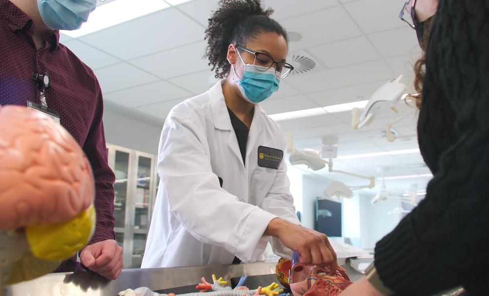 Alison Nesbitt in a lab setting surrounded by other people observing a dissection model